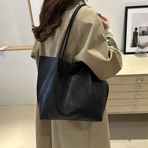 Borsa tote nera intrecciata da donna, indossata da una modella con un classico trench
