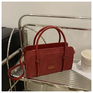 Detailed close-up of a red corduroy handbag with leather handles and decorative patch