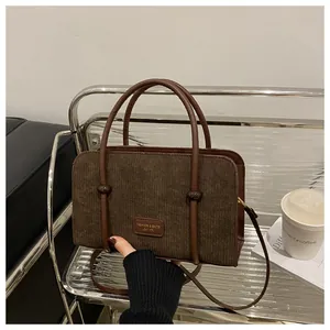 Detail of dark brown corduroy handbag featuring leather handle and a fashion brand tag