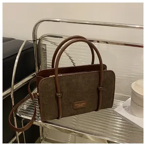 Detailed close-up of dark brown corduroy handbag with leather handles on a glass table