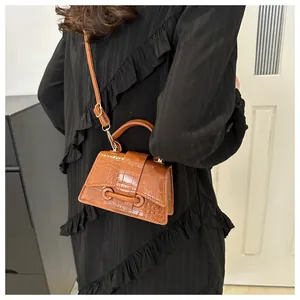 Detail van een bruine mini vierkante tas met krokodillentextuur, handvat en riem