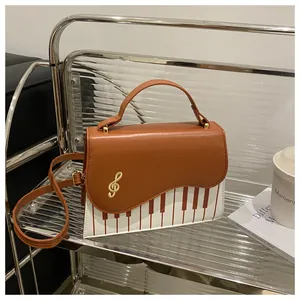 Detail of piano key pattern crossbody bag with golden treble clef metal logo on the flap