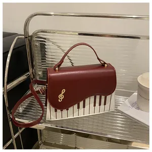 Detail of burgundy and white piano-themed bag with golden G-clef charm and keyboard print