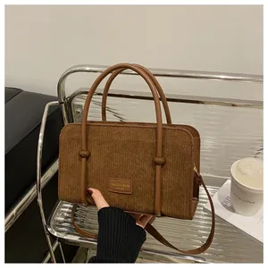 Detail of brown corduroy handbag featuring leather patch logo and round handles