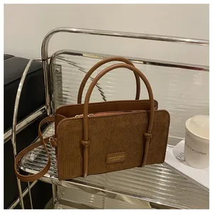 Detail of brown corduroy handbag featuring round leather handles and fashion logo plate