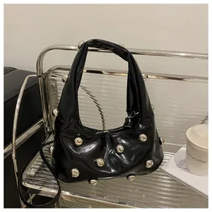 Detail of black glossy handbag featuring large silver studs and metallic hardware decoration