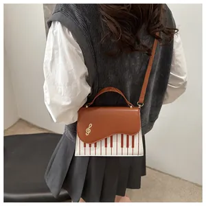 Detail of piano-themed bag with golden treble clef clasp and brown strap on model