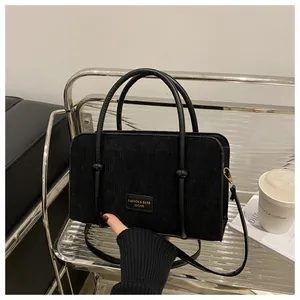 Close-up of black corduroy handbag featuring leather handles and metal fashion logo plate