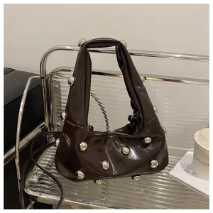 Detail of dark brown glossy leather handbag with silver metallic rivets on a silver shelf