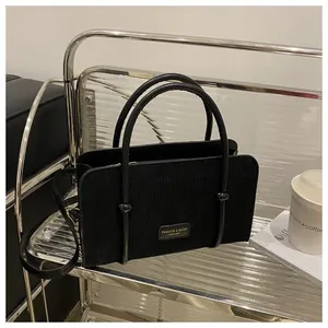 Detailed view of black corduroy handbag with dual top handles and gold-lettered leather patch