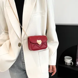 Sac rouge matelassé avec fermoir cœur doré et chaîne sur un costume blanc