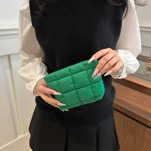 Neceser acolchado verde de nailon sostenido por una modelo en un ambiente minimalista