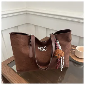 Detail of a brown suede tote bag with teddy bear charm and woven rope decoration