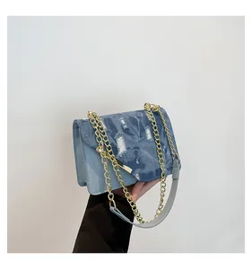 Detail of light blue leather and frayed denim patchwork bag with gold chain strap