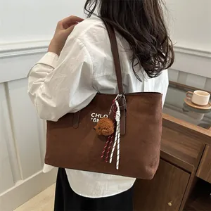 Brown suede tote bag with shoulder strap and plush bear charm for daily commute