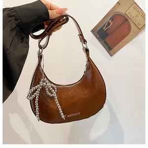 Close-up of brown patent leather crescent bag with silver beaded bow and Fashion text