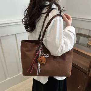 Brown suede tote bag with plush charm and woven rope detail shown on a female shoulder
