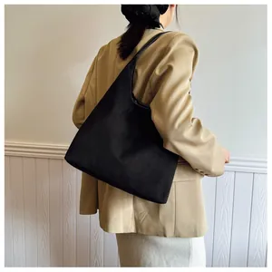 Close-up of a large black matte tote bag worn with a khaki blazer in a minimalist setting