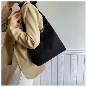 Side view of a minimalist large black tote bag worn with a beige blazer suit