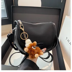 Dettaglio della borsa a tracolla in pelle nera con finiture dorate e ciondolo mostro di peluche