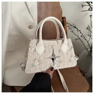 Detail of floral embroidery and star metallic emblem on woven straw handbag with leather handle