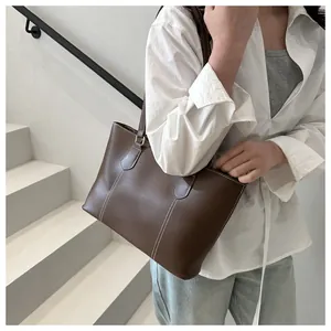 Close-up of brown leather tote bag featuring detailed white contrast stitching and shoulder straps