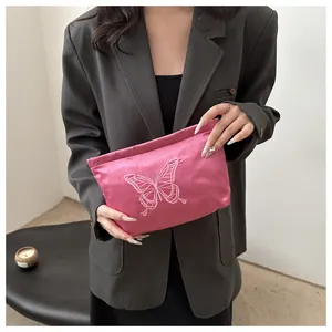 Detail of pink satin pouch with butterfly embroidery held by a model in a grey suit