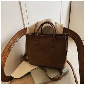 Detailed view of brown canvas tote bag with metal rivets and layered pockets on a chair