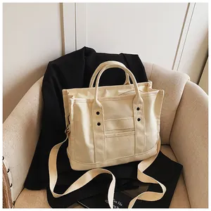 Close-up of cream canvas tote bag with black rivets and adjustable shoulder strap on sofa