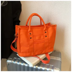 Detail of orange canvas tote bag with black rivets and adjustable strap on a suitcase