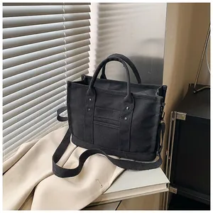 Detail of black canvas tote bag showing double handles and metallic rivets in sunlight