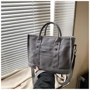 Detail of grey canvas tote bag with metal rivets, fabric straps and textured surface