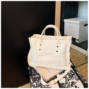 Close-up of cream canvas tote bag with black rivets and adjustable fabric shoulder strap