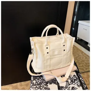 Close-up of white canvas handbag with adjustable strap and rivet accents on books