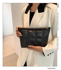 Close-up of black quilted puffer clutch bag with gold zipper held by a model in a suit