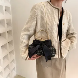 Elegant black evening bag with a satin bow and golden metal handle on tweed outfit