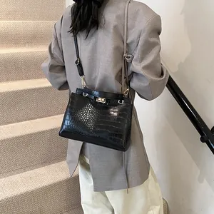 Sac à main noir avec motif crocodile et fermoir doré porté par un mannequin chic