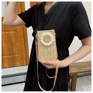 Vertical straw woven crossbody bag with white daisy flower detail worn by a model