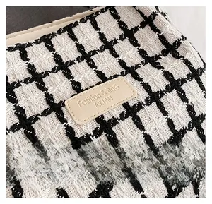 Macro detail of black and white checkered tweed fabric with leather logo patch for tote bag