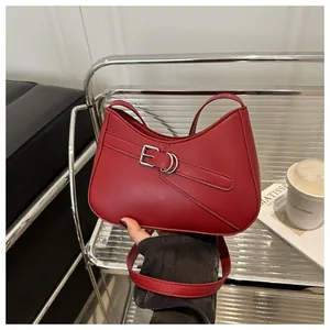 Detalle del bolso de hombro en cuero mate rojo con hebilla decorativa y bandolera