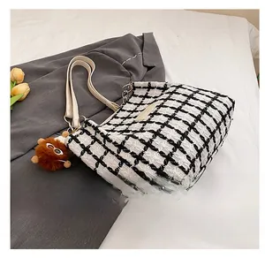 Side view of black and white plaid wool tote bag with white leather straps and plush charm