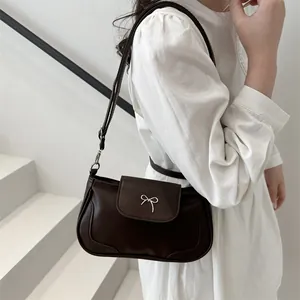 Vintage brown shoulder bag with silver bow accent on elegant model in white dress