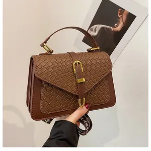 Detail of dark brown handbag with croc-embossed flap and black-white woven strap