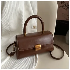 Detail view of a vintage brown leather bag with a metallic square clasp on a textured fabric