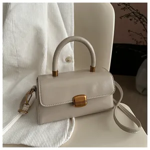 Close-up of cream square handbag showing gold metal buckle and pleated leather texture