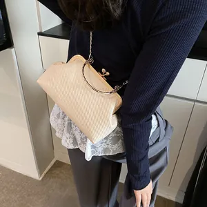 Beige woven clutch bag with gold metal frame and chain strap shown on model shoulder