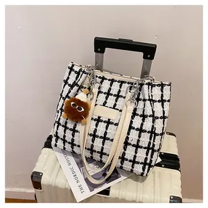 Detail of checkered tweed tote bag with leather straps and furry doll charm on suitcase