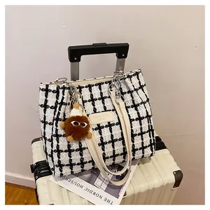Close-up of black and white checkered tweed tote bag with plush monster charm on suitcase