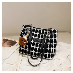 Detail of plaid tweed tote bag with leather strap, silver chain and plush pompom charm
