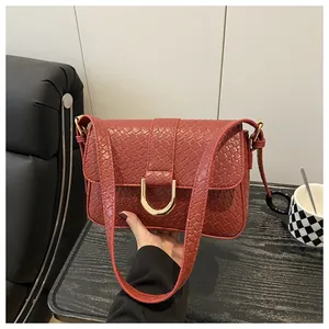 Close-up of burgundy embossed leather shoulder bag with golden horseshoe buckle detail
